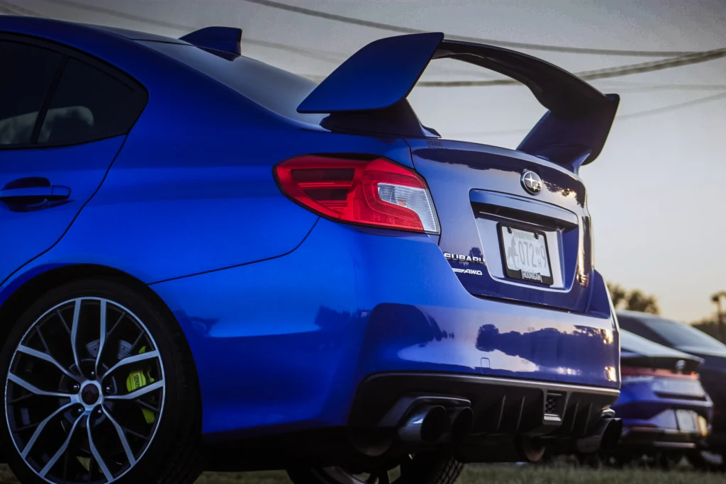 Blue Subaru WRX STI rear with large spoiler and black multi-spoke wheel in outdoor car meet