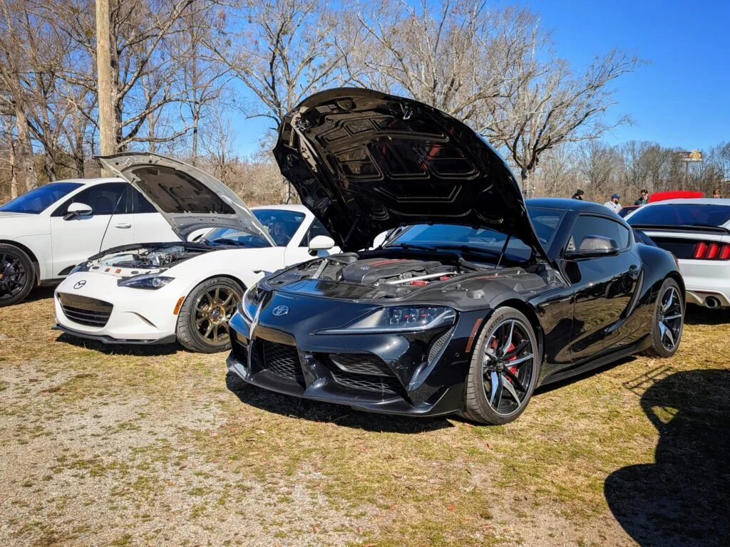 Black Toyota Supra front 3/4 with hood open at a car meet outdoors on a sunny day