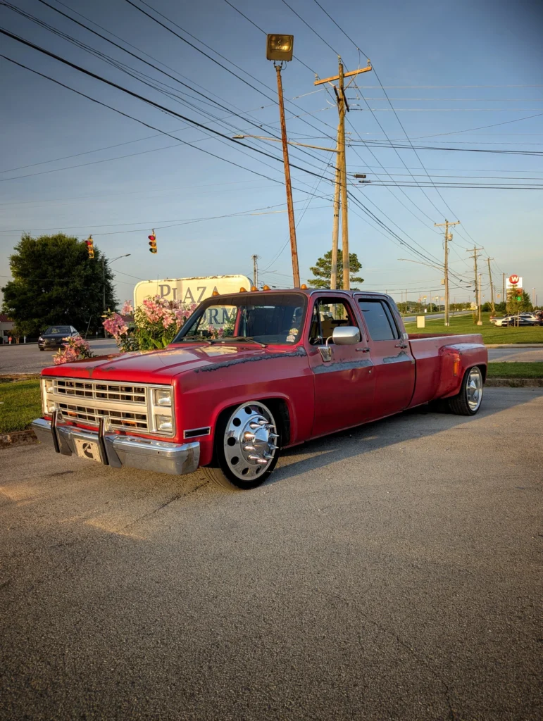 Red Chevrolet pickup truck with extended cab and custom wheels parked in a lot near a Plaza sign and utility poles