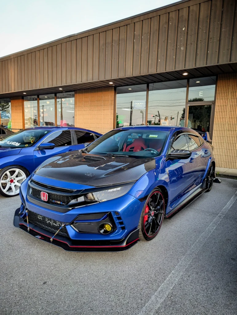 Blue Honda Civic Type R with carbon fiber hood parked in front of a commercial building with reflective windows