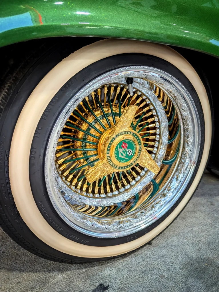 Close-up of a green and gold wire spoke car wheel with whitewall tire and green fender above
