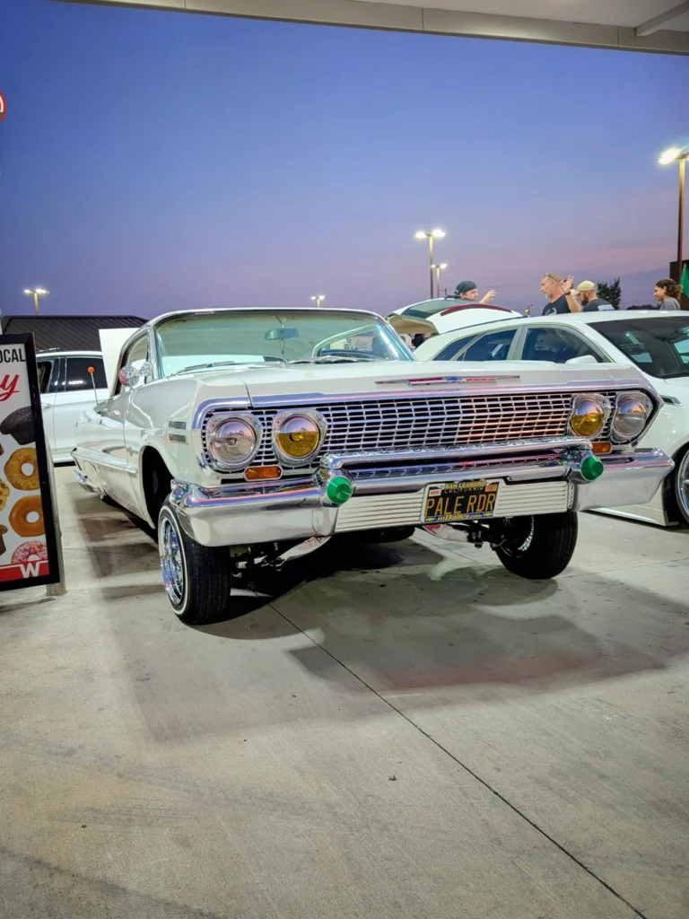 White Chevrolet Impala parked outside at dusk with people and other cars nearby