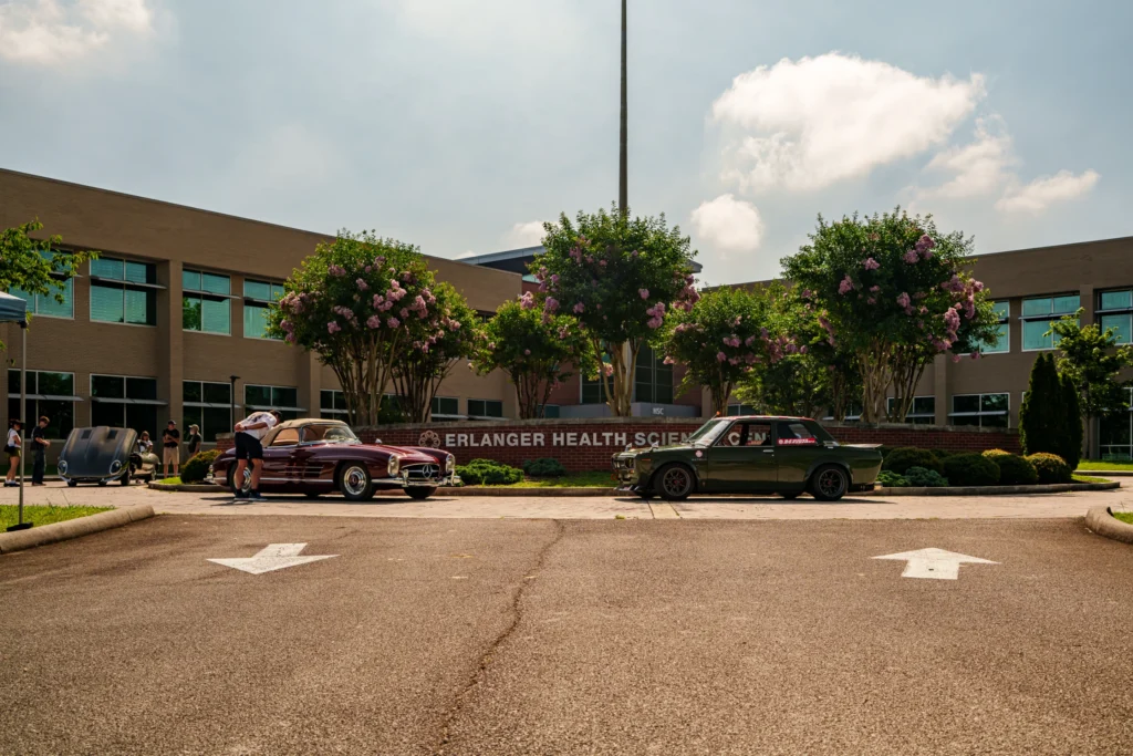 Maroon Mercedes-Benz 300SL and green Nissan Skyline parked in front of Erlanger Health Science Center on a clear day