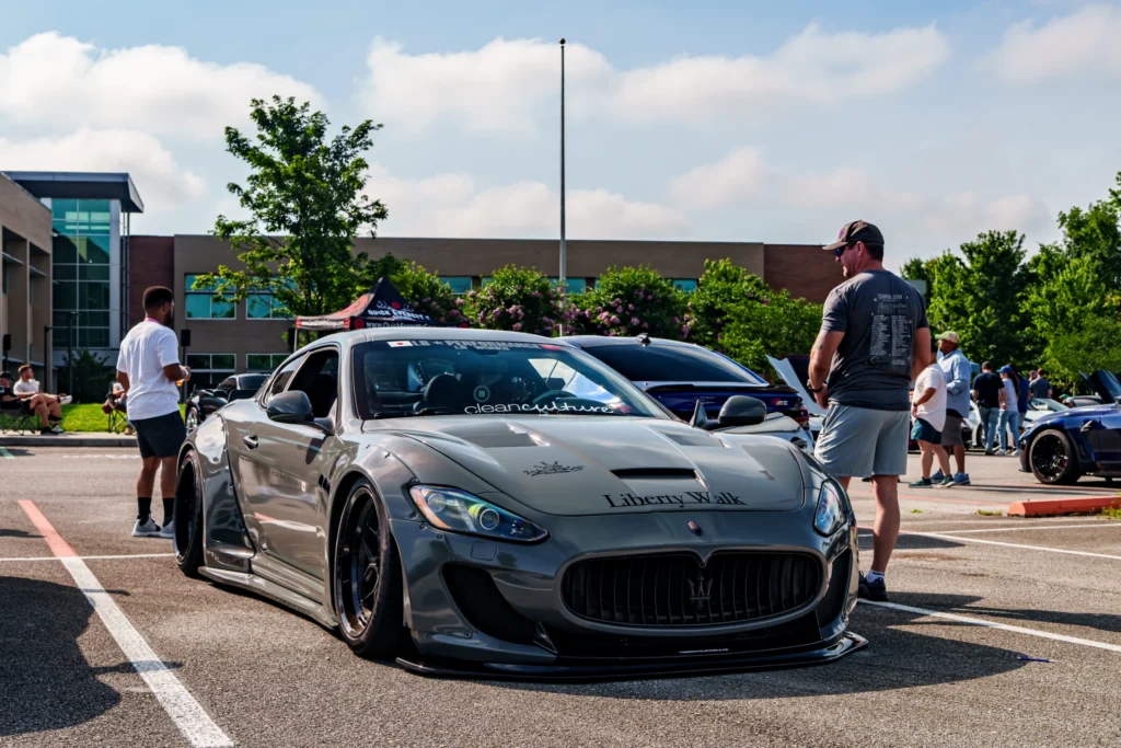Gray Maserati GranTurismor with wide fenders parked at outdoor car event with people and other cars in background