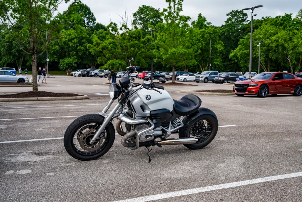 Silver BMW motorcycle parked in a lot with cars and people in the background at an outdoor event