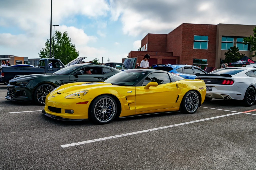Yellow Chevrolet Corvette ZR1 and dark green Chevrolet Camaro ZL1 parked side by side at an outdoor car event with other vehi