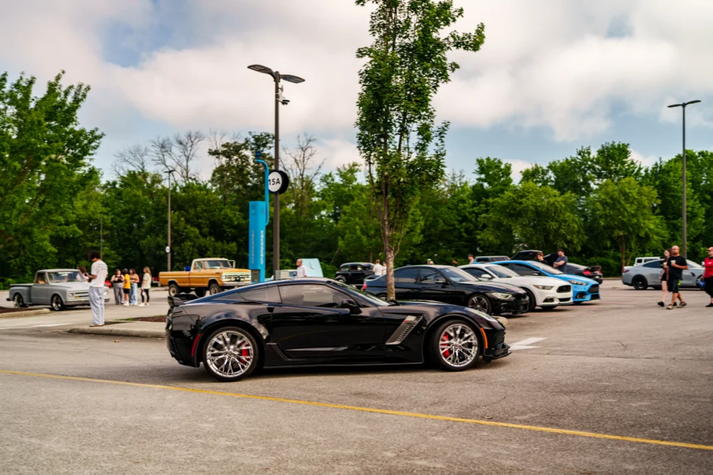 Black Chevrolet Corvette parked in a lot with other cars and people in the background at an outdoor event