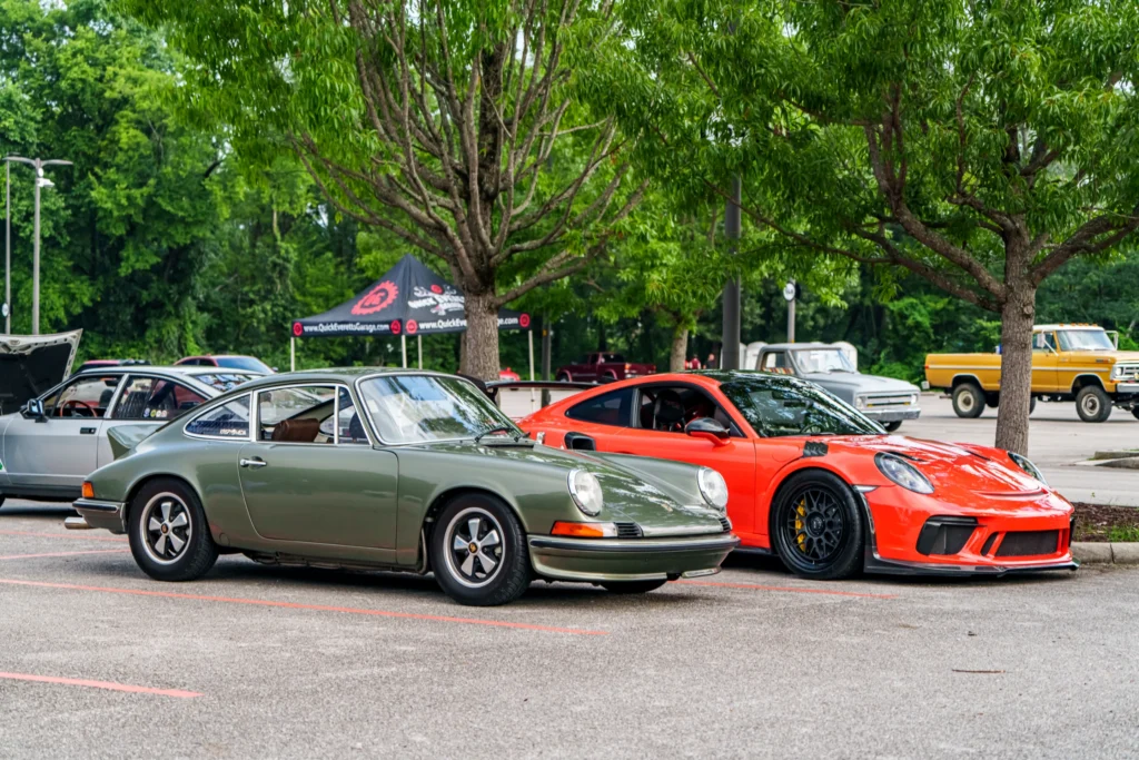 Green Porsche 911 and red Porsche 911 GT3 parked side by side at an outdoor car event