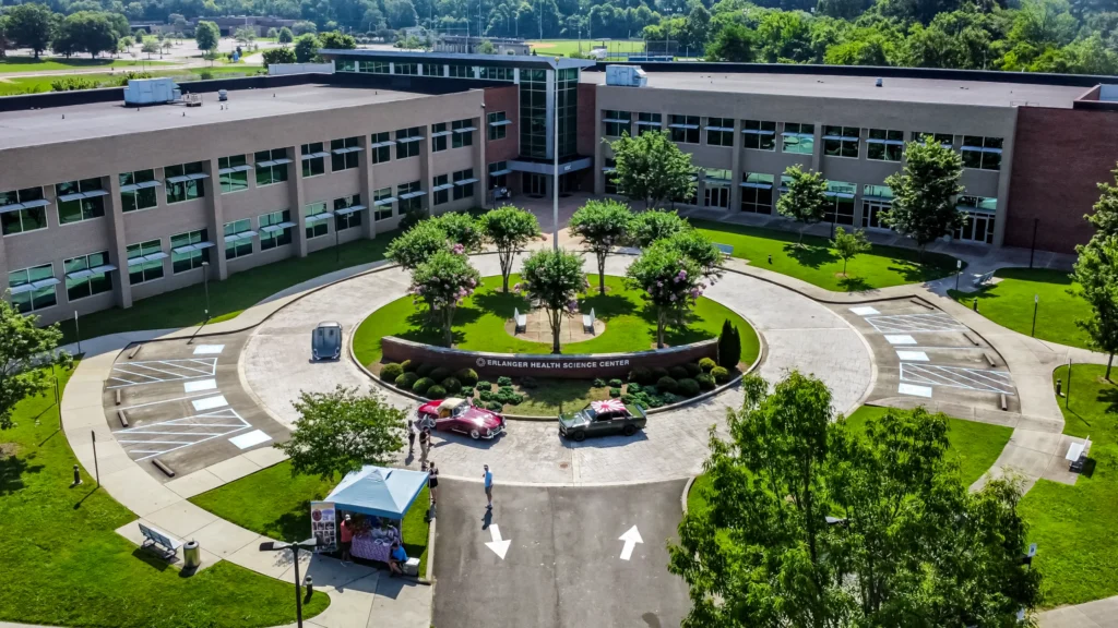 Two vehicles parked by a circular driveway in front of Erlanger Health Science Center with people nearby and tents set up