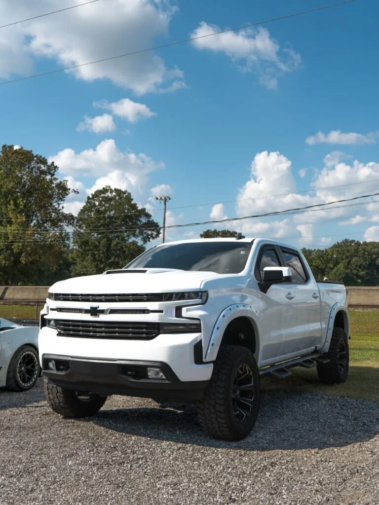White Chevrolet Silverado pickup truck parked on gravel with trees and blue sky in background