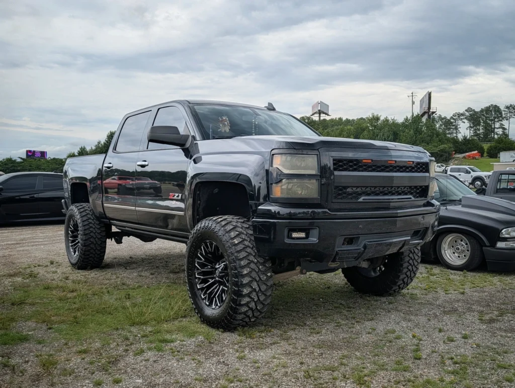 Black Chevrolet Silverado Z71 lifted truck parked on gravel with other vehicles and cloudy sky in background
