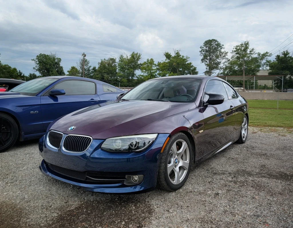 Blue BMW 3 Series parked next to a blue Ford Mustang GT at an outdoor car event on a cloudy day