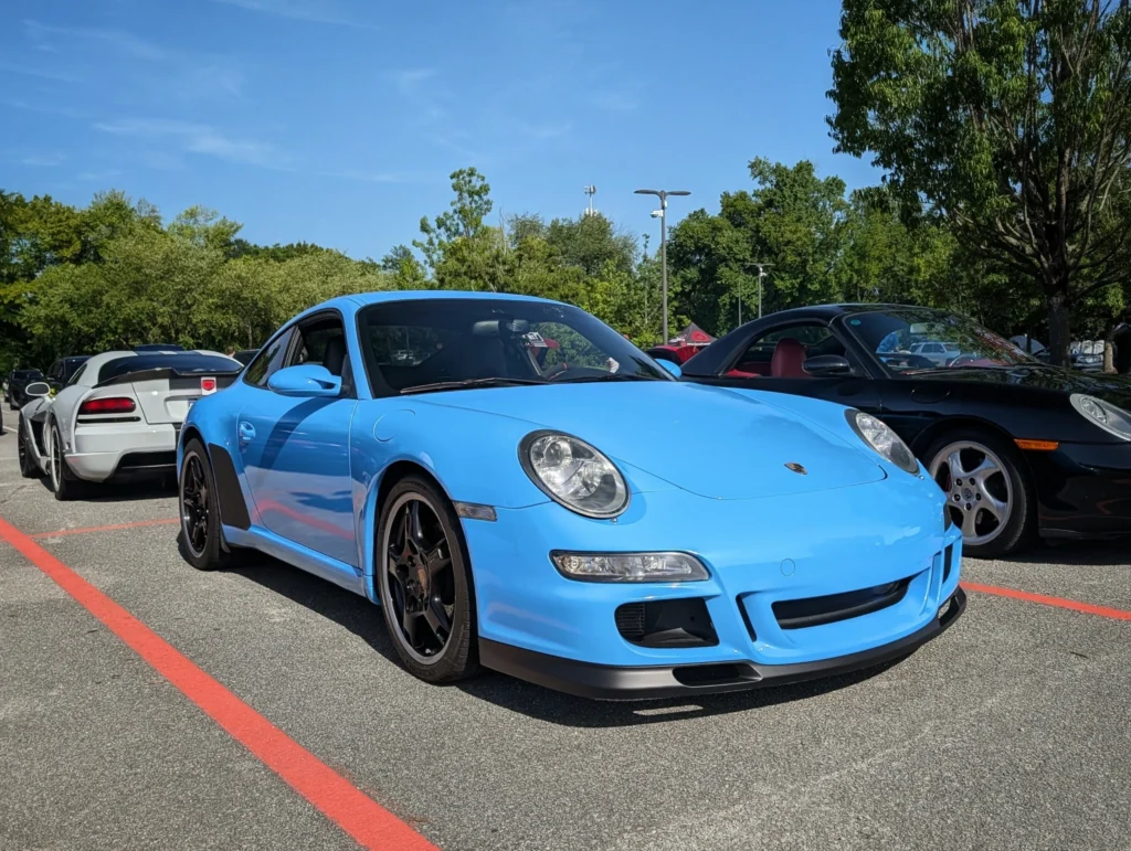 Light blue Porsche 911 GT3 parked in a lot with several other sports cars on a sunny day