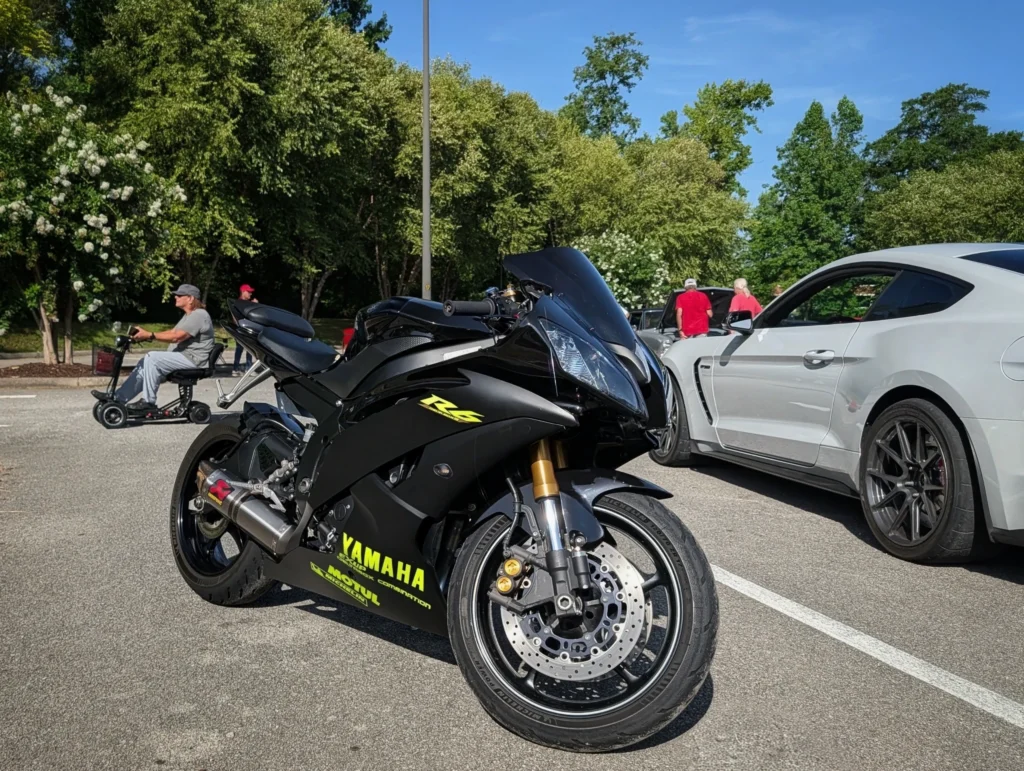 Black Yamaha R6 motorcycle parked next to a white coupe with trees and people in the background