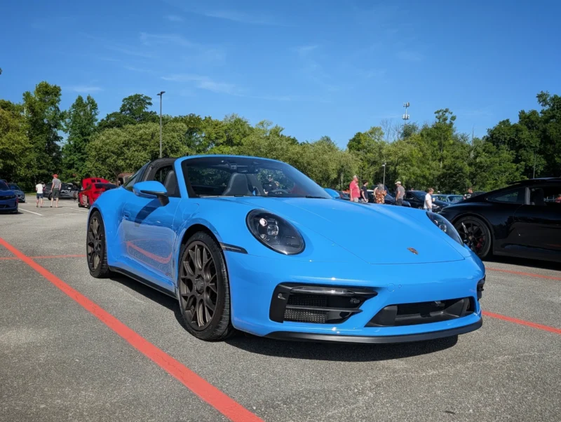 Blue Porsche 911 Targa parked at an outdoor car event with other vehicles and attendees in the background