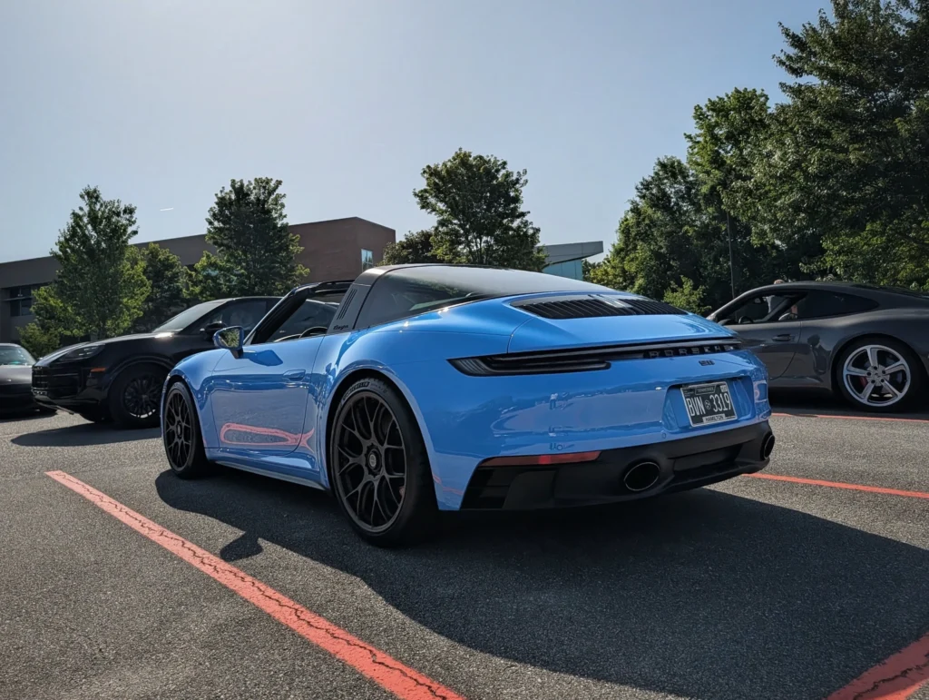 Blue Porsche 911 Targa and black Porsche Cayenne parked side by side in a lot with trees and building in background