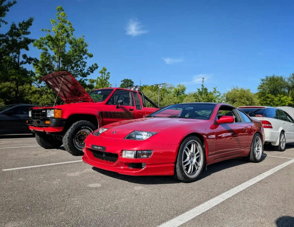 Red Nissan 300ZX and red Toyota pickup truck with hood open, parked outdoors under clear sky with surrounding trees