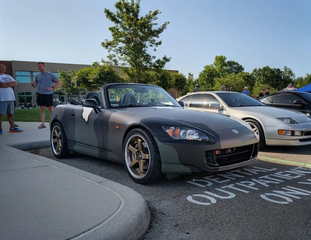 Gray and black Honda S2000 convertible parked next to other cars with people in background at a car meet