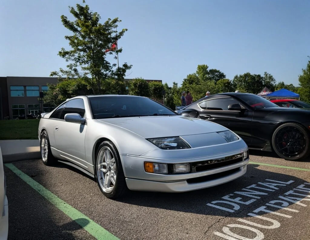 Silver Nissan 300ZX and black Porsche Cayman parked side by side at an outdoor car event