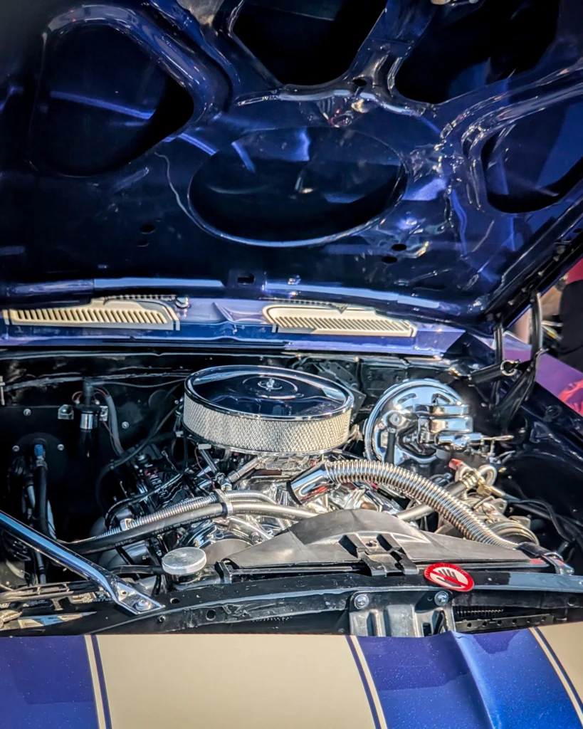 Close-up of a car engine bay with blue underside hood and chrome air filter housing visible
