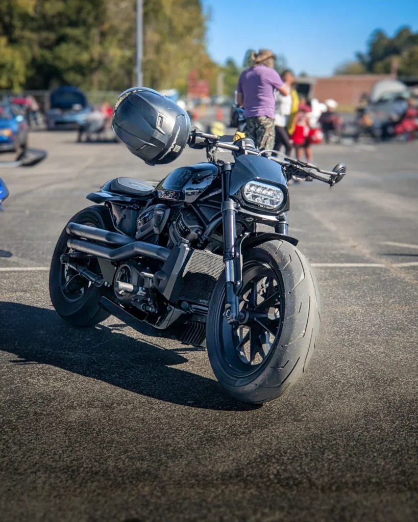 A black Harley-Davidson Sportster S is parked at an outdoor car show with a helmet hanging from its handlebar.