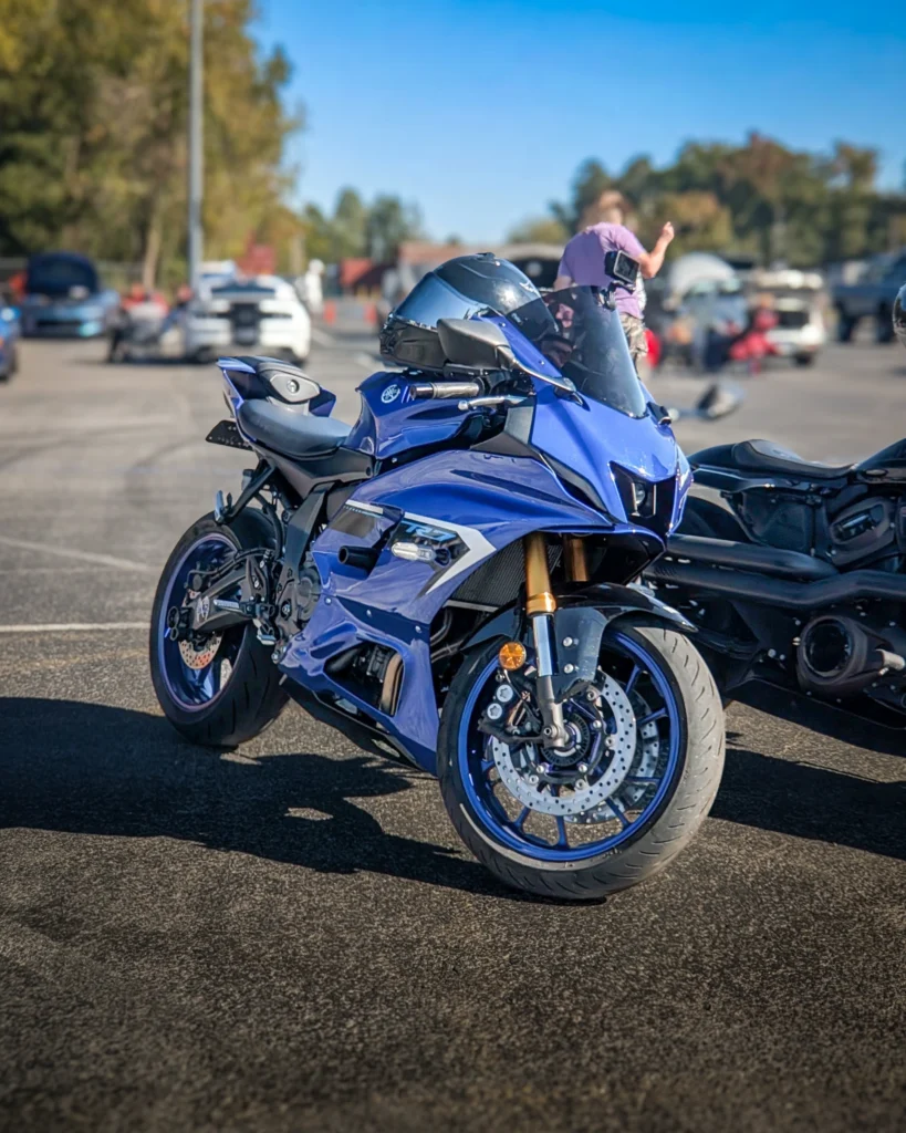 Blue Yamaha R7 motorcycle with helmet parked on asphalt at car event with white cars and people in background