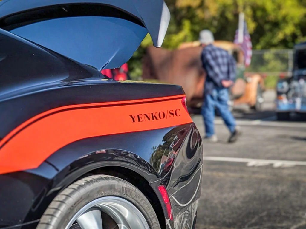 Close-up of rear section of a Chevrolet Camaro with orange Yenko/SC stripe and open trunk lid at outdoor event