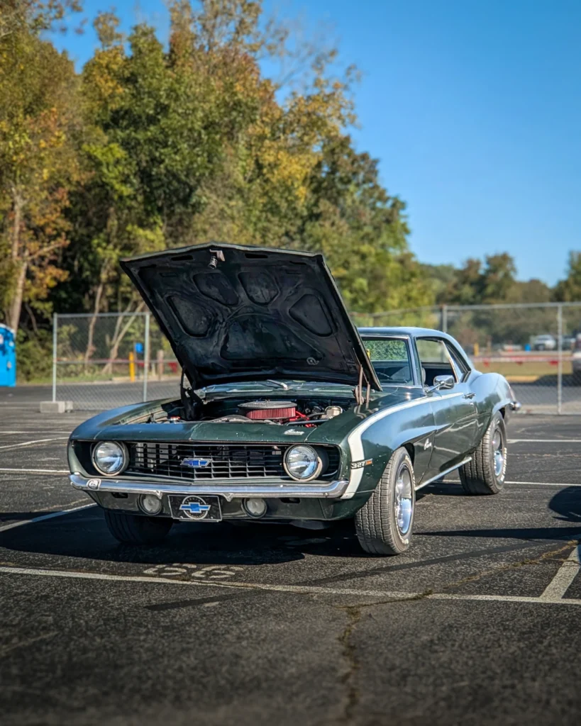 Dark green 1969 Chevrolet Camaro with hood open in an outdoor parking lot during a clear day