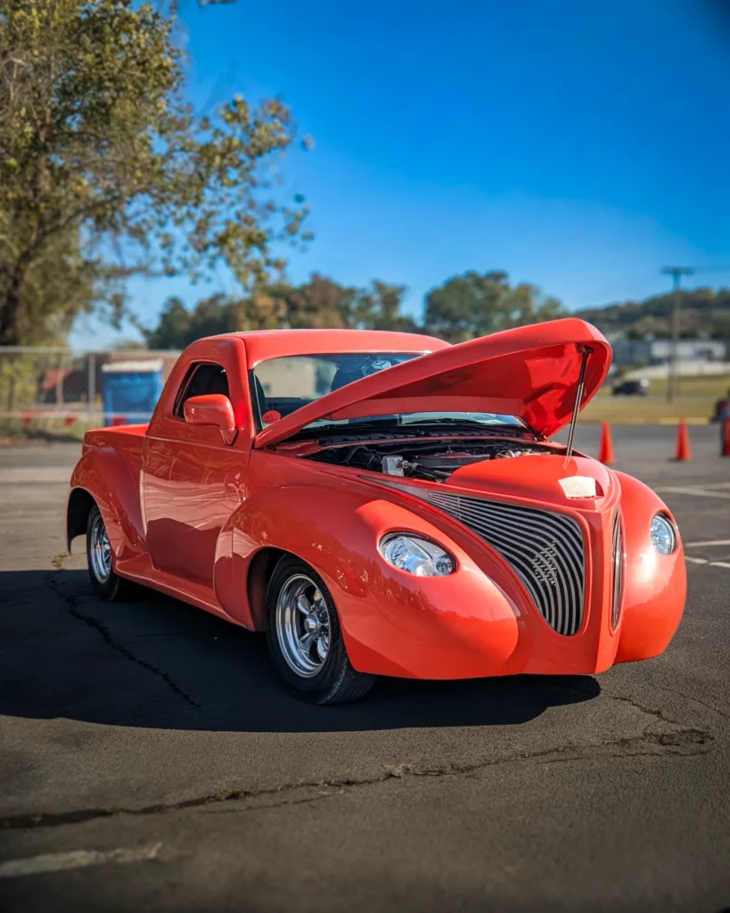 Red custom pickup truck with open hood parked outdoors under clear blue sky