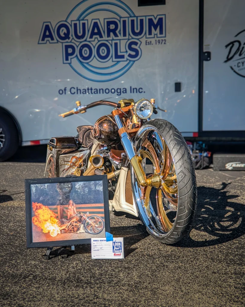 Custom motorcycle with gold and chrome parts parked in front of a trailer with 'Aquarium Pools' signage