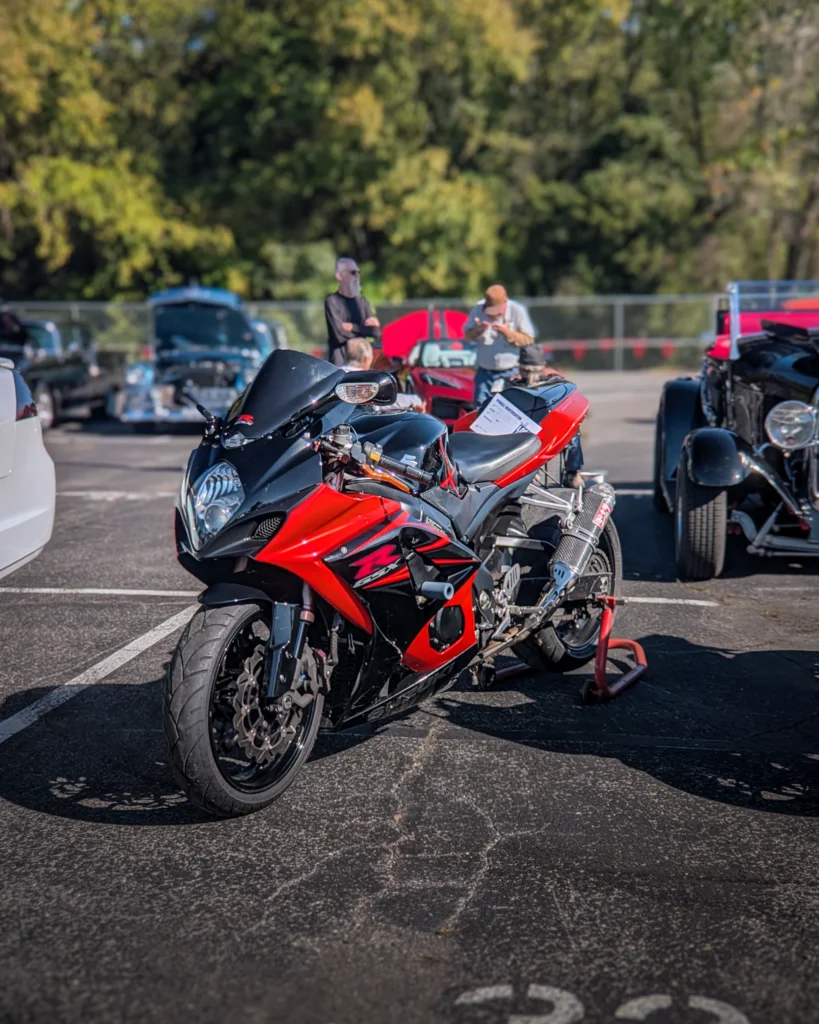 Black and red Suzuki GSX-R motorcycle parked in lot with other vehicles and people in background at car event