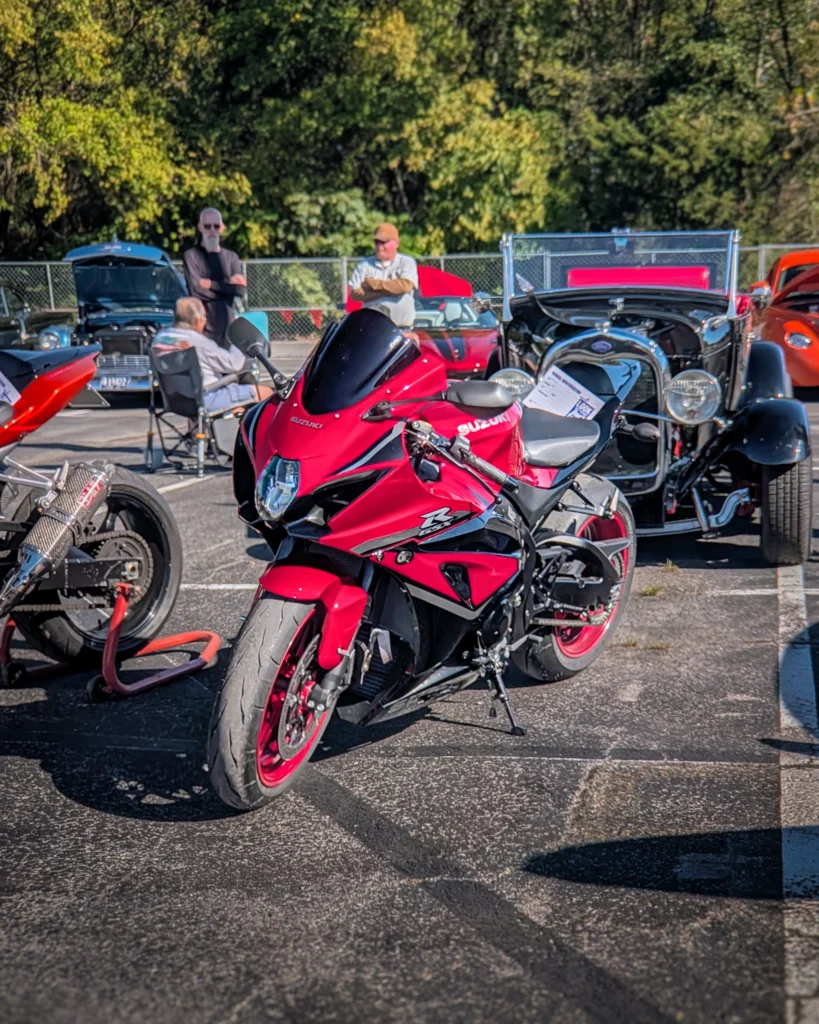 Red Suzuki GSX-R motorcycle parked at a car event with various vintage cars and people in the background