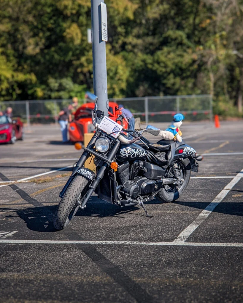 Black Honda Shadow Phantom with white flame decals parked in a lot with red car and people in background
