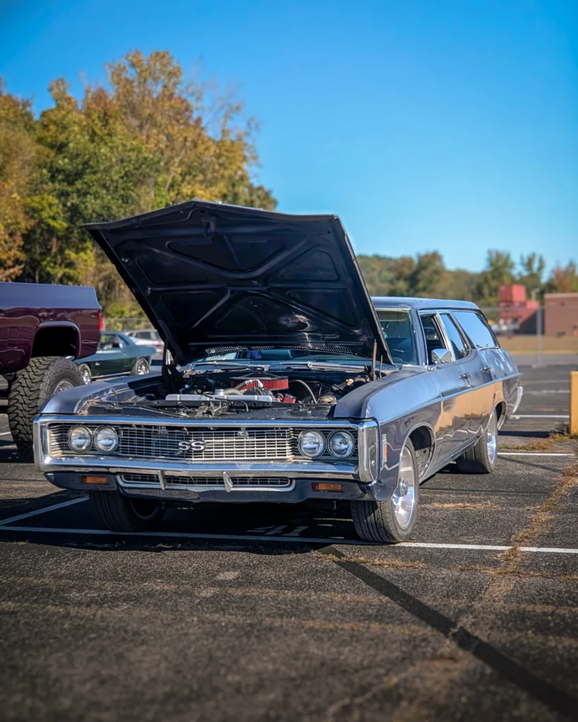Black Chevrolet Impala wagon with its hood open in a parking lot during a car event on a clear day