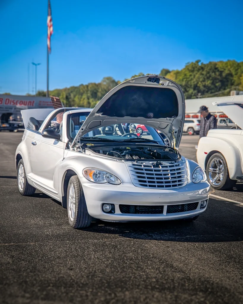 Silver Chrysler PT Cruiser convertible with hood open in outdoor parking lot at car event