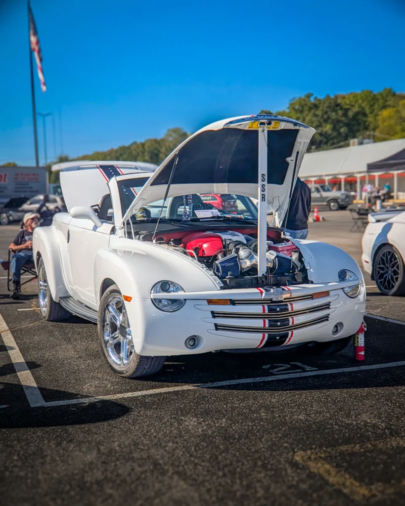 White Chevrolet SSR convertible with hood open showing engine at outdoor car event on sunny day