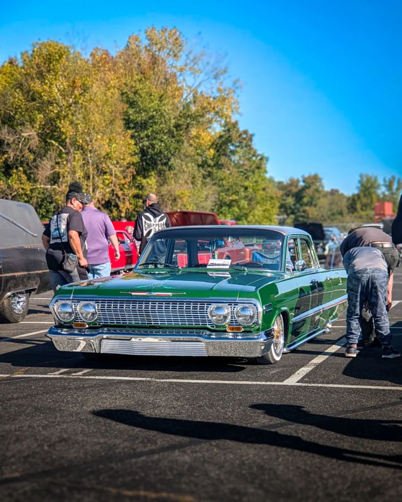 Green Chevrolet Impala parked outdoors with people and other vehicles nearby under a clear blue sky