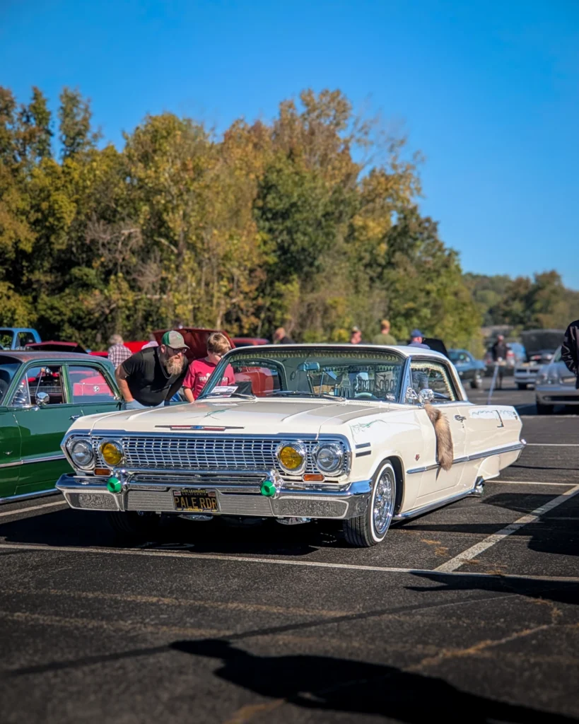 White Chevrolet Impala convertible parked in an outdoor car event with people and other vehicles in the background