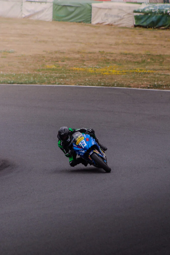 Motorcyclist in black and green gear leaning into a turn on a blue race motorcycle with number 73 on a track.