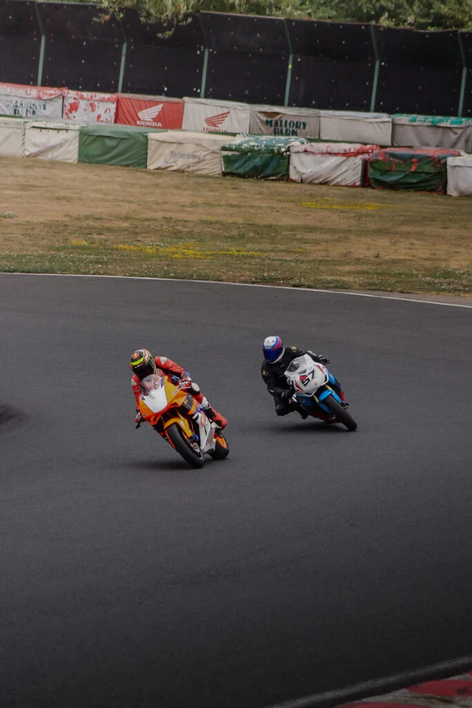 Two racing motorcycles on a curved asphalt track with protective barriers in the background
