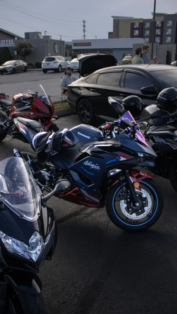 Three parked sport motorcycles including a black and red Kawasaki Ninja and a black car in the background with people nearby