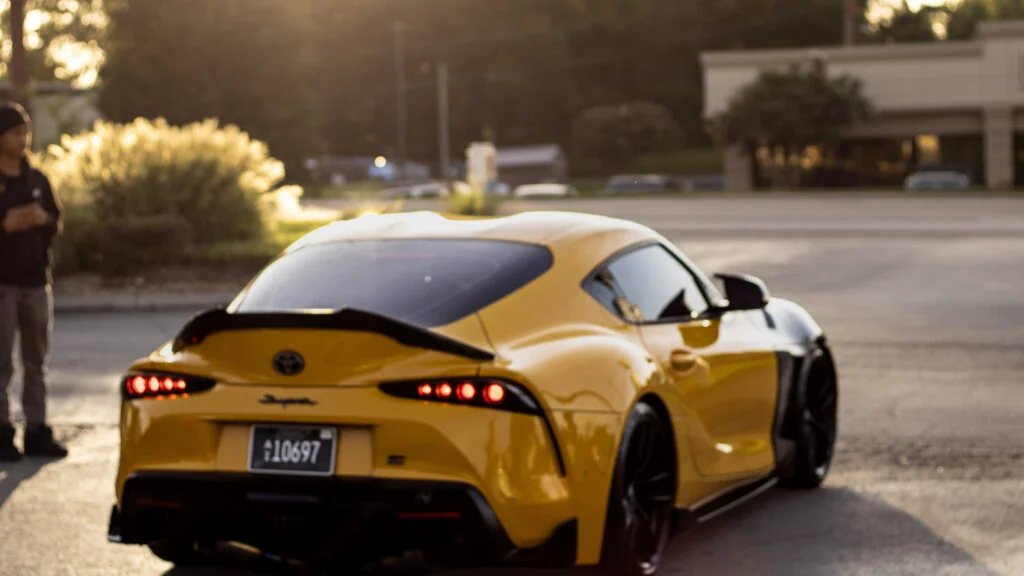 Yellow Toyota Supra parked outdoors near a person on a sunny late afternoon