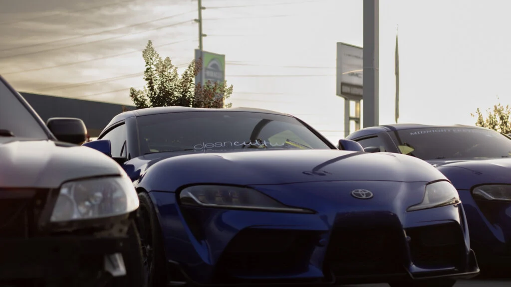 Blue Toyota Supra parked between two other vehicles at an outdoor car event during sunset