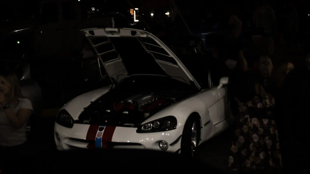 White Dodge Viper with hood open and blue and red stripes, shown at night with people around