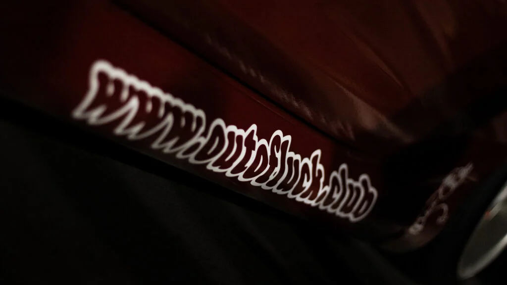 Close-up of white script decal on red vehicle body panel in low light