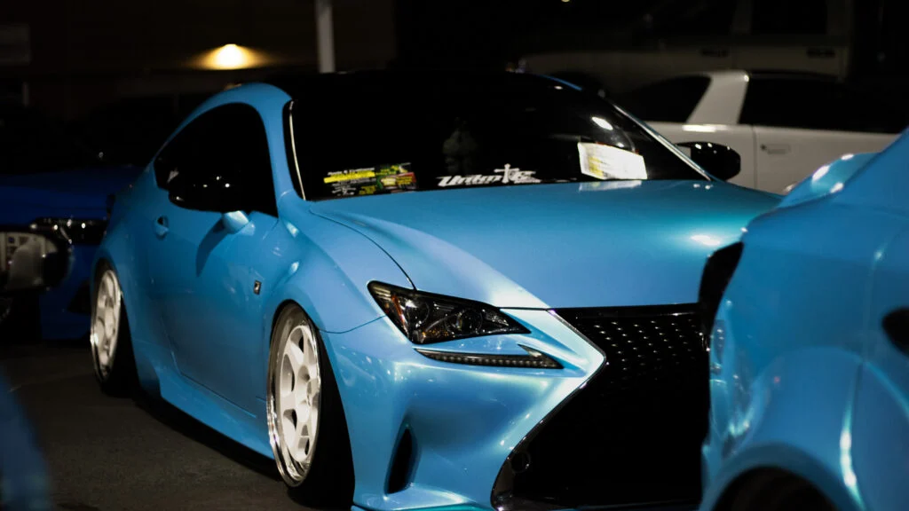 Blue Lexus RC200t F Sport parked at night with lowered stance and white rims, other vehicles visible in background