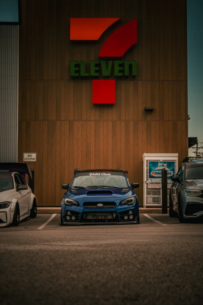 Blue Subaru WRX parked in front of a 7-Eleven store alongside other vehicles in a parking lot