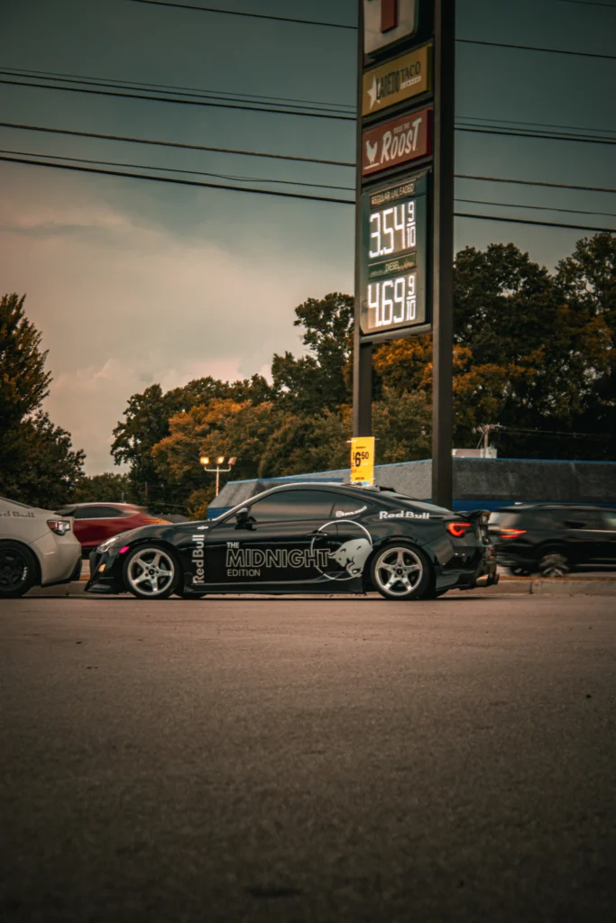 Black Toyota GR86 with The Midnight Edition and Red Bull decals parked next to other vehicles under a signboard with gas pric