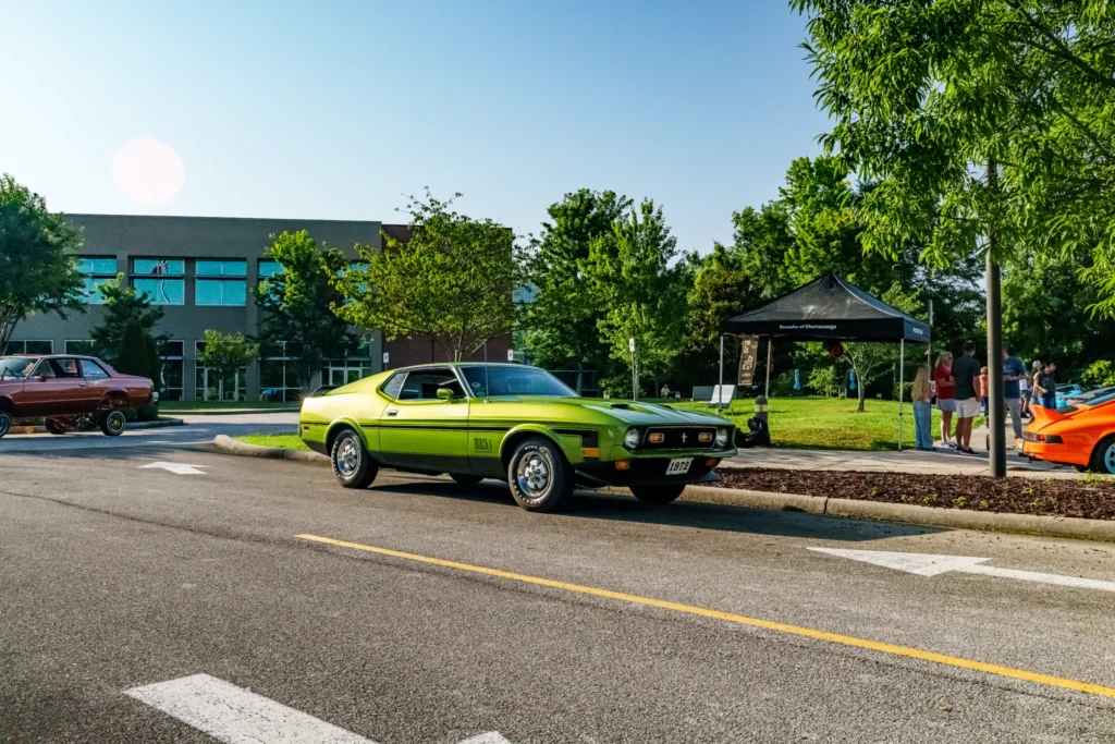 Green 1972 Ford Mustang Mach 1 parked on a street at a car event with people and trees in the background