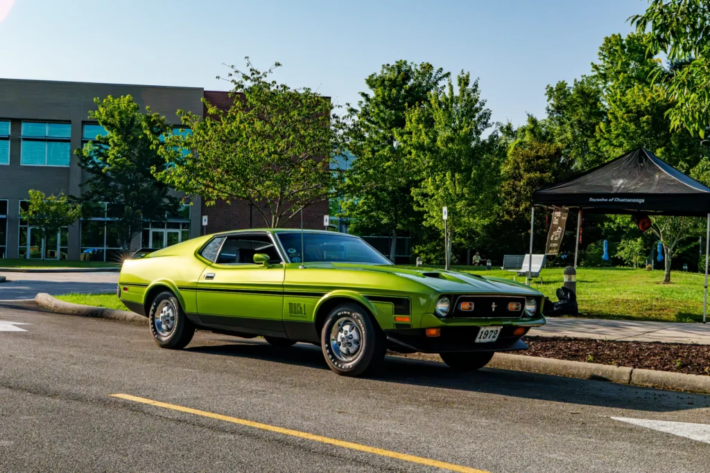 Green Ford Mustang Mach 1 parked in a lot near trees and a Porsche of Chattanooga tent